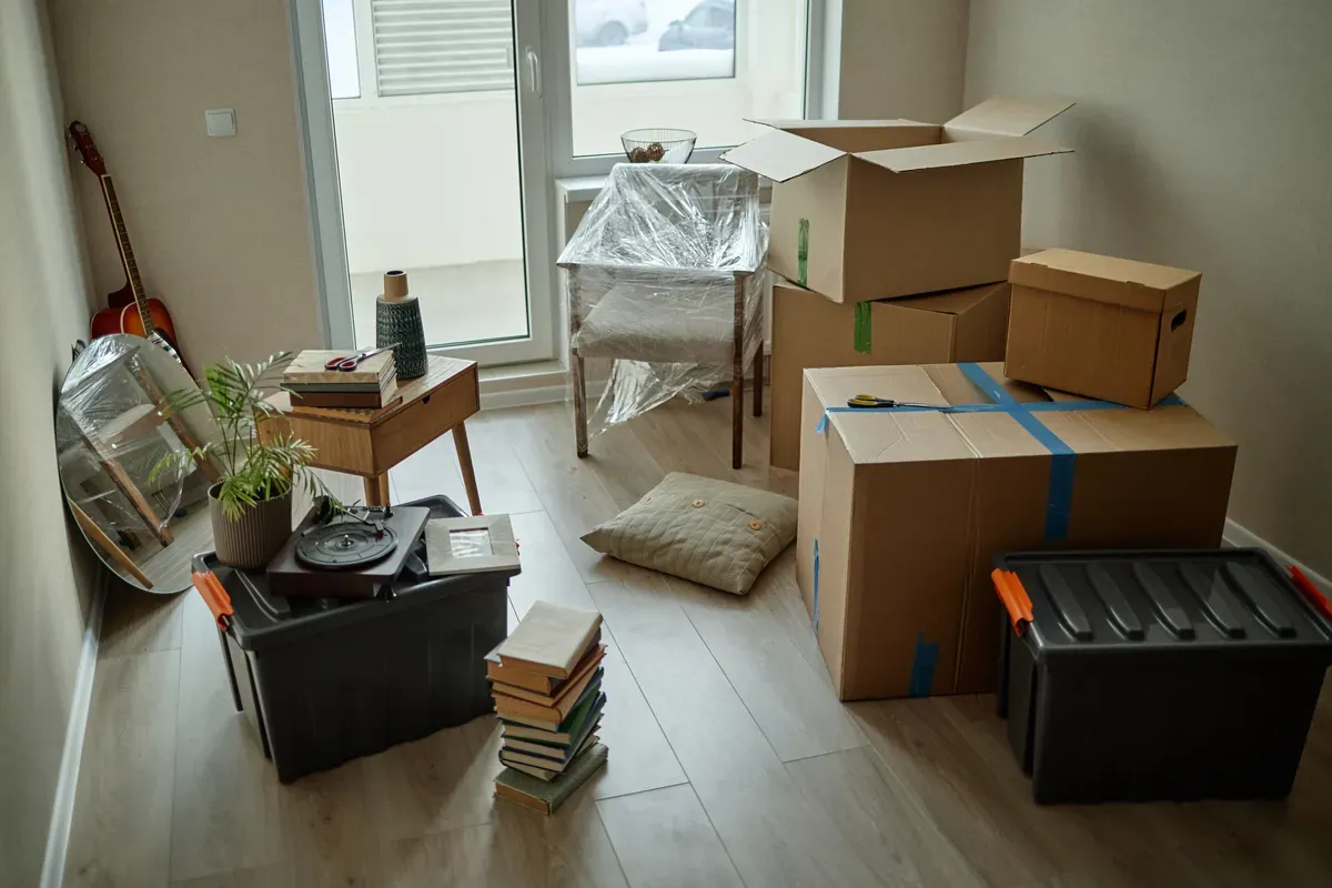 A guitar, books, and several boxes sit on a wood floor ready to be moved into storage.
